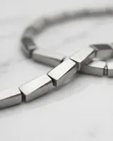 Collar de acero compuesto por una serie de piezas rectangulares articuladas y un dije central de forma cúbica.
