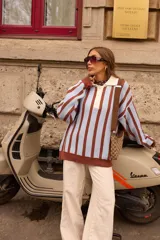 Buzo tejido de punto con diseño a rayas verticales en color celeste y marrón chocolate. Presenta un cuello polo con solapa en color crema y cierre frontal de tres botones, mangas largas de corte holgado y terminaciones en tejido acanalado.