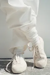 Zapatilla deportiva color blanco con detalles en gamuza y diseño de talonera elástica, cordones al tono y suela plana dentada.
