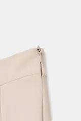 Bermuda larga de tiro medio en color beige, con diseño de pinzas frontales y costuras marcadas. Presenta un corte amplio y cierre lateral con cremallera oculta.