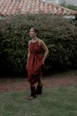 Vestido largo color marrón de crepé plissé, con escote halter adornado con detalles de perlas, silueta fluida y lazo ajustable en la cintura.