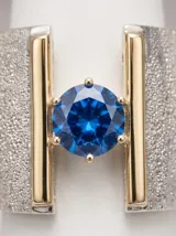 Anillo ancho de plata y oro con textura granulada y piedra circonia central de color azul.