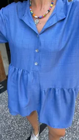 Vestido corto de manga larga con volados, color lavanda, con cuello camisero y botones frontales.