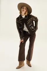 Campera de lana merino hervida en color crudo, con diseño de cuello camisero, cierre frontal de botones y bolsillos frontales. Presenta bordados artesanales con motivos geométricos en tonos marrón y azul en el frente, espalda y mangas.