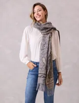 Bufandón de tejido suave con estampado de arabescos en tonos grises y beige, con terminación de flecos en los extremos.
