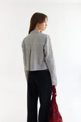 Blusa blanca de algodón con cuello mao y tablas verticales en el frente que crean un efecto de volumen. Presenta cierre frontal con botones y mangas largas.