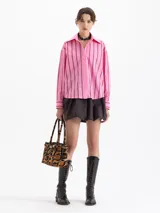 Camisa blanca de poplin con fit holgado, cuello con broche metálico y mangas largas con puños abotonados. Presenta un patrón de rayas verticales formadas por bordados de boquitas.