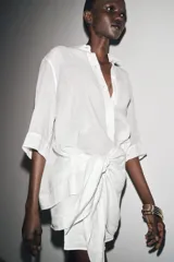 Camisa de color mostaza, con cuello solapa, manga corta y bajo recto. Cierre frontal con botones.