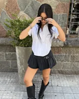 Minifalda tableada de jean color negro, con diseño de tiro bajo y detalle de cinturón integrado con hebilla metálica plateada.