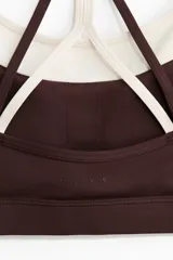 Top deportivo en tejido funcional de color marrón con tirantes dobles en color crudo y diseño de superposición. Cuenta con escote redondo y copas con relleno extraíble.