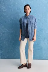 Sobrecamisa de denim de calce amplio y color azul, con cuello clásico, cierre frontal con broches metálicos y bolsillos delanteros con solapa.