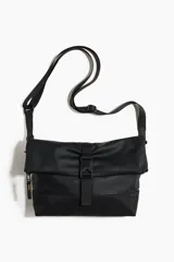 Bolso cruzado negro de tejido revestido, con compartimento principal con cremallera, solapa plegable, correa bandolera ajustable y cierre central con hebilla de plástico.