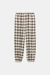 Pantalón bombacho de tiro alto con estampado de cuadros en tonos crudo y marrón. Presenta cintura elástica ajustable con cordón y bajos elásticos.