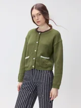 Cardigan de algodón grueso color rojo, con cuello redondo, cierre frontal de botones grandes y bolsillos cuadrados en el frente. Presenta detalles de pelo sintético en el cuello y los bolsillos, y logo bordado en uno de los bolsillos.