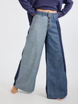 Pantalón ancho de jean, tiro alto, con cierre de botones frontales. Presenta un diseño de patchwork con paneles de denim en diferentes tonos de azul (claro, medio y oscuro).