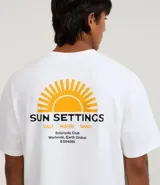 Remera de algodón blanca, corte relajado (relaxed fit), con cuello redondo y manga corta. Presenta un pequeño estampado frontal en el pecho con un sol estilizado y el texto "Sun Settings".