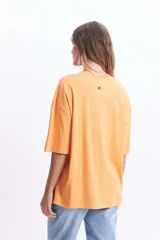 Remera oversize de algodón color naranja con cuello redondo y manga corta. Presenta un estampado lineal de tres flores en color blanco.