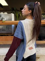 Sweater de punto con diseño de ochos y estilo patchwork, combinando paneles en colores terracota, marrón y beige. Presenta cuello redondo, mangas largas y costuras decorativas a la vista.