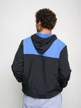 Canguro negro con capucha y medio cierre, marca Umbro, modelo Urban. Detalles en azul en el logo, interior de la capucha y ribete de los bolsillos.