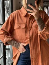 Sobrecamisa de pana color ladrillo, con cuello clásico, cierre frontal de botones, bolsillos plaqué con tapa en el pecho y mangas largas.