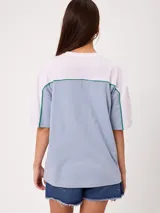 Remera oversize de manga corta marca Rusty, modelo Rocca, en combinación de colores celeste, blanco y detalles en verde. Presenta estampado frontal con el logo de la marca y diseño de bloques de color.