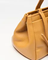 Cartera tipo tote XL confeccionada en símil cuero de textura granulada color habano. Cuenta con doble asa de mano, detalles de correas decorativas con hebilla en los laterales y un charm colgante en forma de corazón. Incluye placa metálica con las iniciales de la marca en el frente.