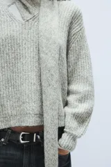 Jersey de punto de corte holgado en color gris jaspeado, con escote en pico y bufanda integrada del mismo tejido. Presenta mangas largas con puños ajustados.