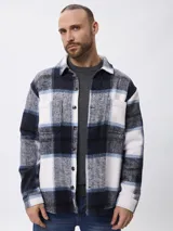 Sobrecamisa de corte recto con estampado de cuadros en tonos azul, blanco y gris. Presenta cuello clásico, cierre frontal con botones, mangas largas con puños abotonados y bolsillos frontales en el pecho.