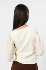 Blusa color manteca de cuello redondo y mangas largas abullonadas con puños elásticos.