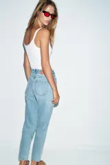 Jeans de denim azul claro lavado, tiro alto, corte Mom Fit con pierna recta y largo tobillero. Presenta cinco bolsillos y cierre frontal con cremallera y botón.