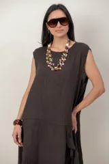 Vestido midi de lino color beige, sin mangas y con cuello redondo. Cuenta con un diseño irregular con detalle de volado vertical a un costado.