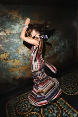 Vestido largo de encaje y transparencias color marrón, con escote profundo halter, frunces en el cuerpo, espalda abierta y tiras largas estampadas para atar al cuello.