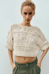 Top cropped de punto con diseño combinado de texturas, cuello redondo y mangas cortas amplias. Presenta una estructura calada con detalles de cintas verticales.