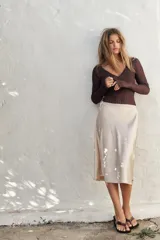 Falda corta tipo pareo, color marrón oscuro, confeccionada en tejido satinado con lazada ajustable en el lateral.