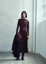 Vestido midi de corte evasé en color marrón oscuro, confeccionado en tejido elástico. Presenta cuello asimétrico, manga larga y diseño sin cierre.