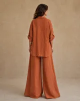 Camisa de lino color terracota, con mangas largas regulables, bolsillo ojal en el pecho, botones de nácar y corte holgado.