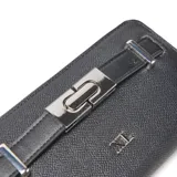 Billetera rectangular XL color negro con textura granulada, cierre perimetral y detalle de tira frontal con herraje metálico plateado.