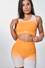 Conjunto deportivo de dos piezas compuesto por un top de cuello redondo y un short de tiro alto, ambos con diseño degradado en tonos naranja y blanco. El top presenta el logo 'bk.' estampado en el frente.