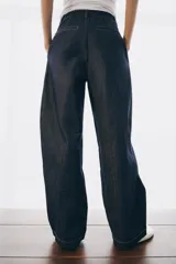 Jeans de tiro alto con corte balloon y largo completo. Presentan cintura con trabillas, bolsillos laterales ocultos, pinzas en el delantero y pespuntes marcados a contraste. Cierre frontal con cremallera, botón y ganchos metálicos.