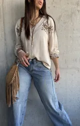 Camisa beige de manga larga con cuello en V, cierre frontal de botones y delicados bordados florales en marrón en la zona del pecho y en los puños.
