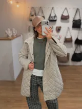 Campera larga de diseño capitoneado con patrón de rombos, color beige. Presenta cierre frontal con botones a presión, cuello alto y mangas largas. Es una prenda versátil ideal para el abrigo en días frescos.