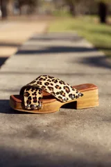 Sandalias de madera con plataforma y taco bajo, con tira ancha de cuero con estampado animal print y apliques de tachas plateadas.