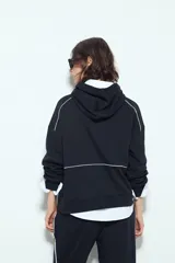 Canguro negro de silueta amplia con capucha integrada y detalles de líneas blancas que recorren el frente y las mangas.