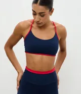 Top deportivo Get Over de corte nadador, confeccionado en microfibra azul marino con detalles en color rojo en los bordes y breteles. Presenta escote en U y copas integradas.