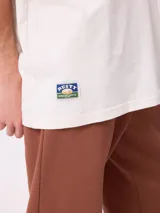 Remera de corte oversize color crema con estampado gráfico en la espalda que muestra un oso, un paisaje natural y el texto 'Stay close to the source'.