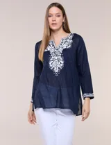 Blusa de corte holgado de inspiración étnica con bordados ornamentales blancos a contraste. Presenta escote en V pronunciado con pechera bordada con motivos arabescos y florales, mangas largas y aberturas laterales en el ruedo.
