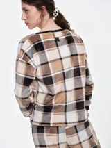 Buzo de dormir de tela fleece con estampado de cuadros en tonos beige, blanco y negro. Presenta cuello redondo y puños en color negro, con un diseño holgado y suave al tacto.