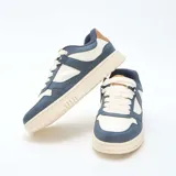 Zapatillas urbanas de diseño tricolor en tonos azul marino, crema y detalles en marrón. Presentan una silueta clásica con cordones gruesos y suela de goma con textura dentada.