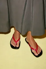 Sandalia plana de piel con suela negra y tira delantera en contraste de color rojo.