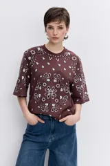 Remera de corte oversize color marrón con estampado tipo bandana en color blanco. Presenta cuello redondo y mangas cortas amplias.